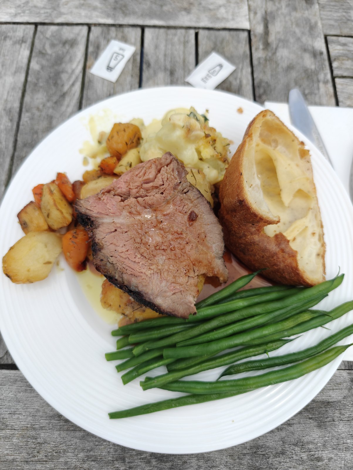 Roast dinner on a white plate with Yorkshire pudding, roast potatoes, green beans and gravy